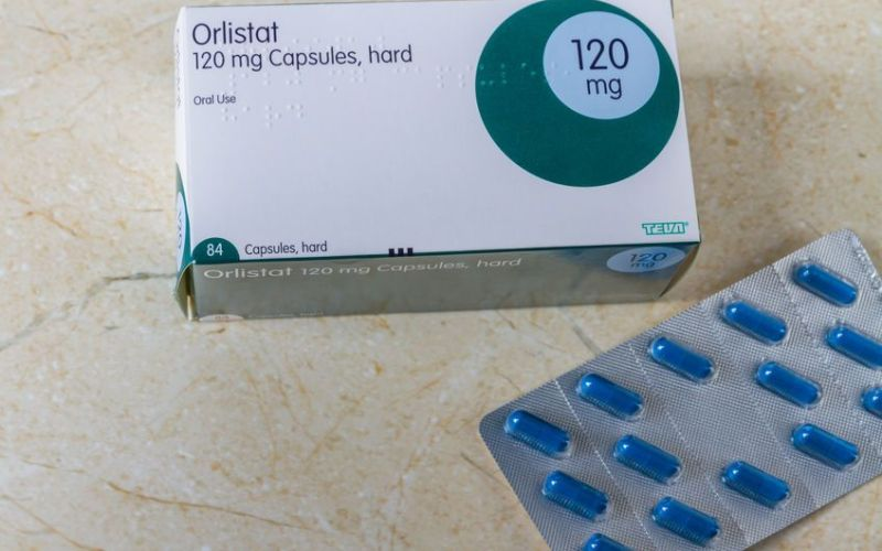 A professional clinical setting showing a bottle of Orlistat 120 mg next to fresh green vegetables